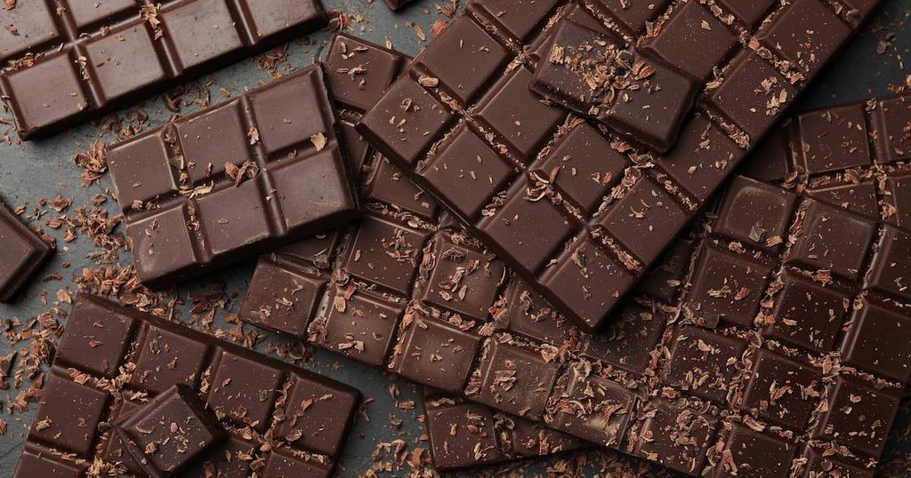 Dark chocolate bars and broken pieces are scattered across a dark gray surface.