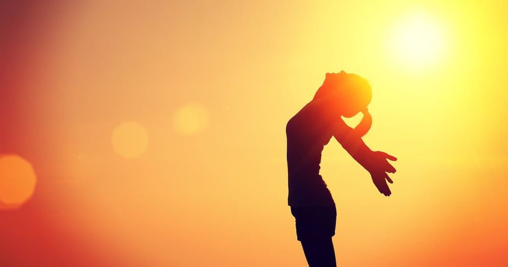 A silhouetted person dances against a vibrant sunset with a prominent sun.