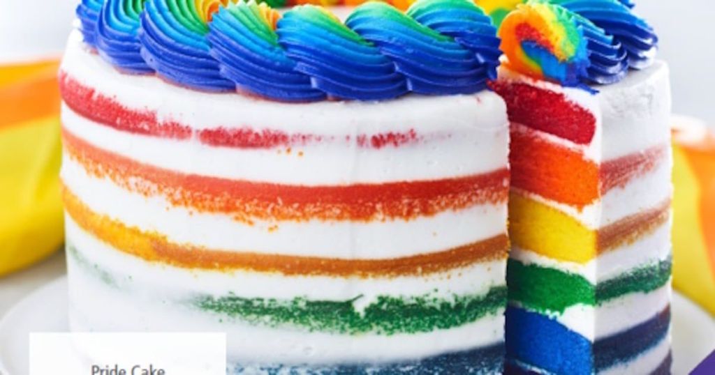 A rainbow-layered cake with blue frosting is decorated with a rainbow swirl and a slice is visible.